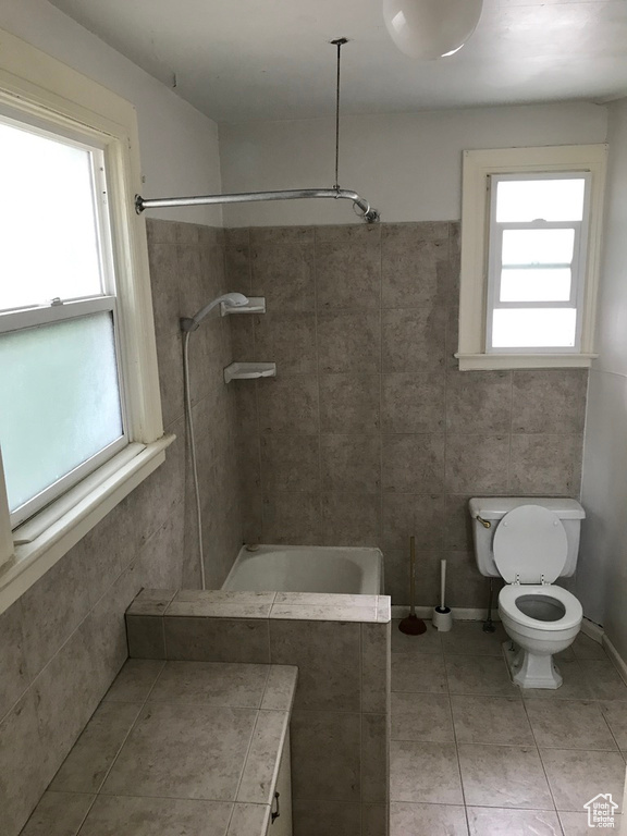 Bathroom featuring tile floors, tiled shower / bath, toilet, and tile walls