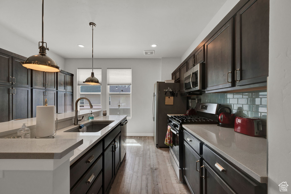 Kitchen featuring sink, light hardwood / wood-style flooring, stainless steel appliances, tasteful backsplash, and pendant lighting
