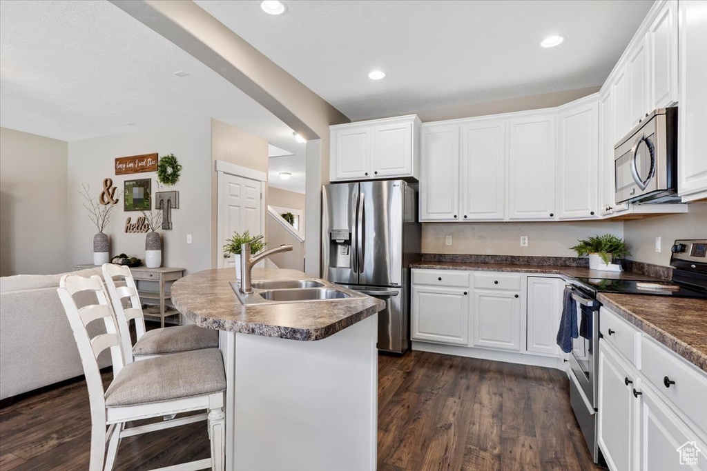 Kitchen featuring white cabinets, appliances with stainless steel finishes, a breakfast bar area, and dark hardwood / wood-style flooring