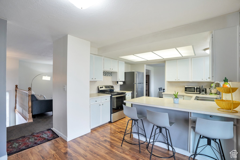Kitchen with white cabinets, wood-type flooring, a breakfast bar area, and appliances with stainless steel finishes