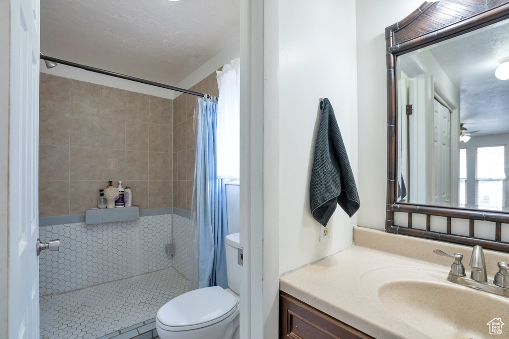 Bathroom with vanity, a shower with shower curtain, ceiling fan, and toilet