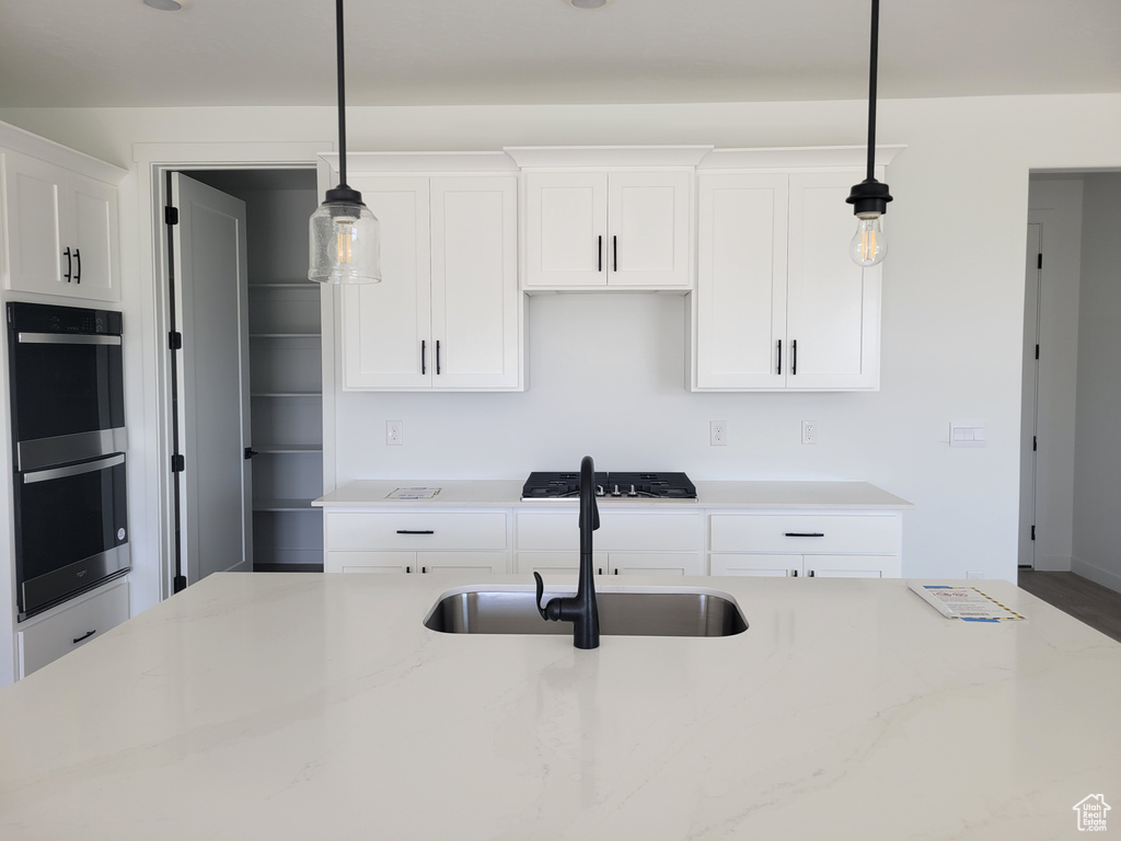 Kitchen featuring pendant lighting, white cabinets, light stone countertops, sink, and stainless steel double oven
