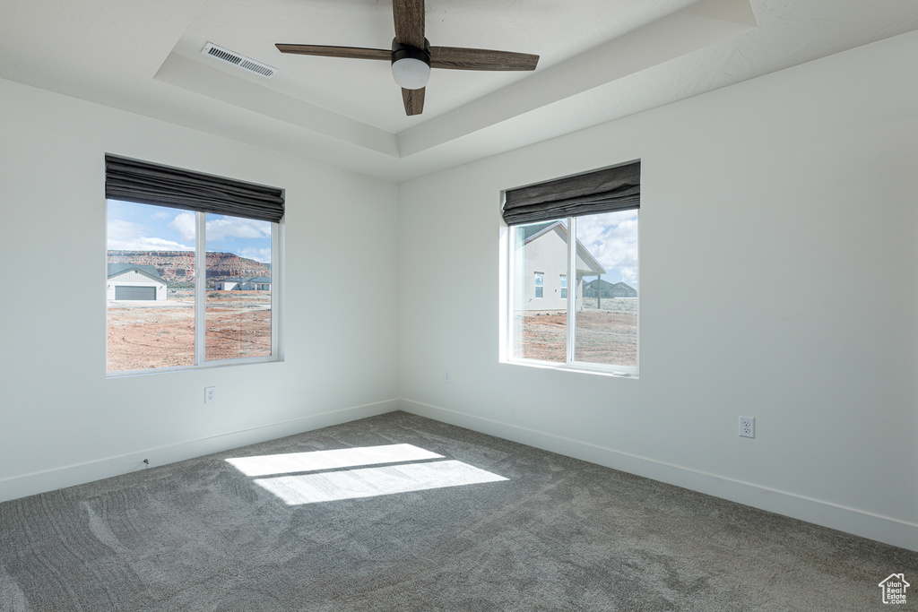 Carpeted empty room featuring a tray ceiling and ceiling fan