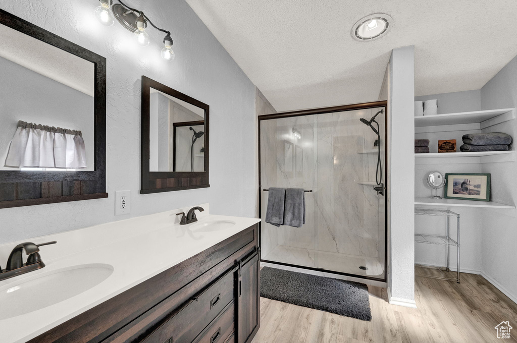 Bathroom featuring a textured ceiling, a shower with shower door, dual vanity, and hardwood / wood-style flooring