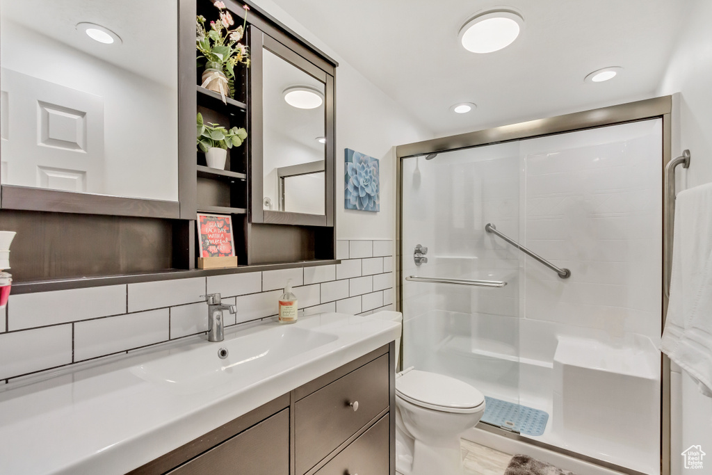 Bathroom featuring a shower with shower door, tile walls, vanity with extensive cabinet space, toilet, and backsplash
