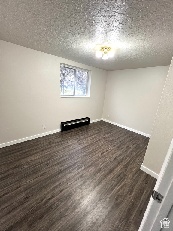 Empty room with a textured ceiling, dark hardwood / wood-style floors, and a baseboard heating unit