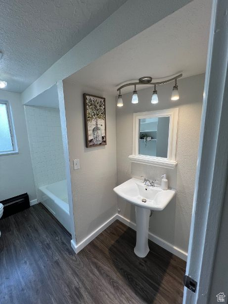Bathroom featuring toilet, a textured ceiling, hardwood / wood-style flooring, rail lighting, and shower / washtub combination