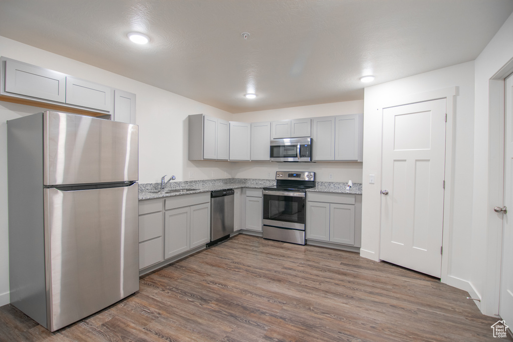 Kitchen featuring light stone countertops, gray cabinets, appliances with stainless steel finishes, dark hardwood / wood-style floors, and sink