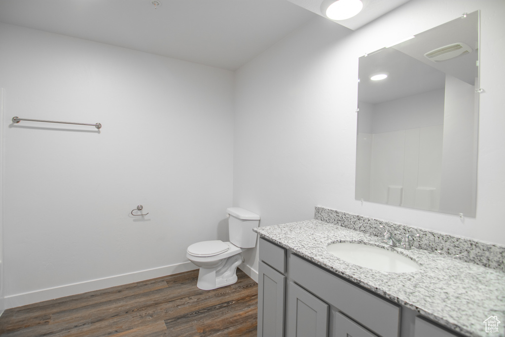 Bathroom with toilet, vanity with extensive cabinet space, and hardwood / wood-style flooring