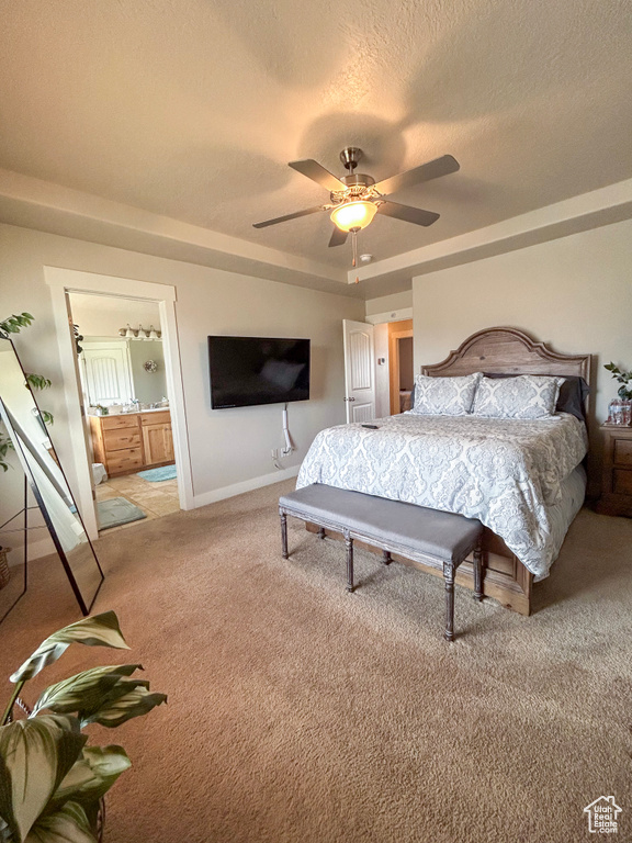 Bedroom with light colored carpet, ceiling fan, ensuite bathroom, a tray ceiling, and a textured ceiling