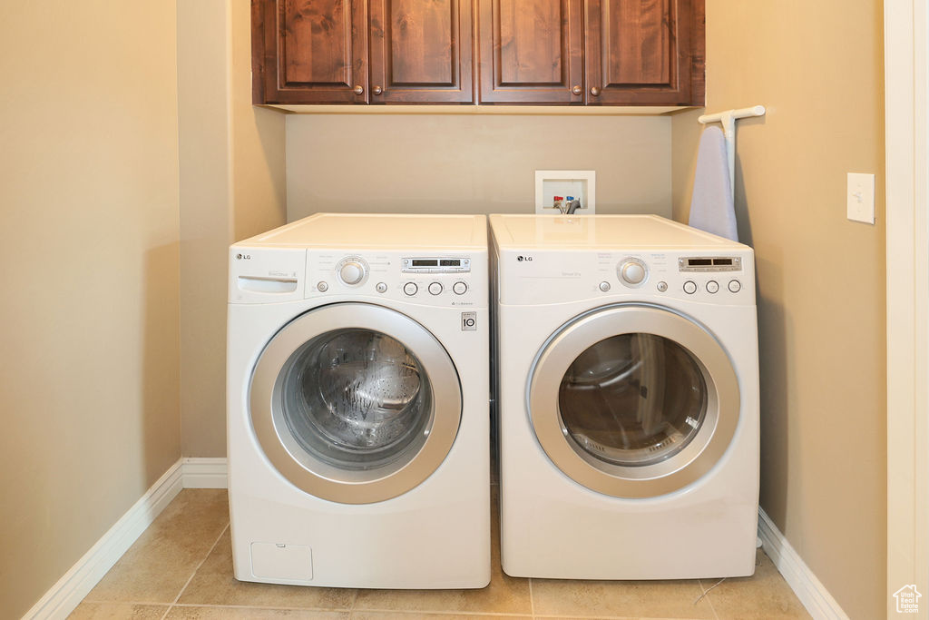 Laundry room with light tile floors, washer and clothes dryer, cabinets, and washer hookup