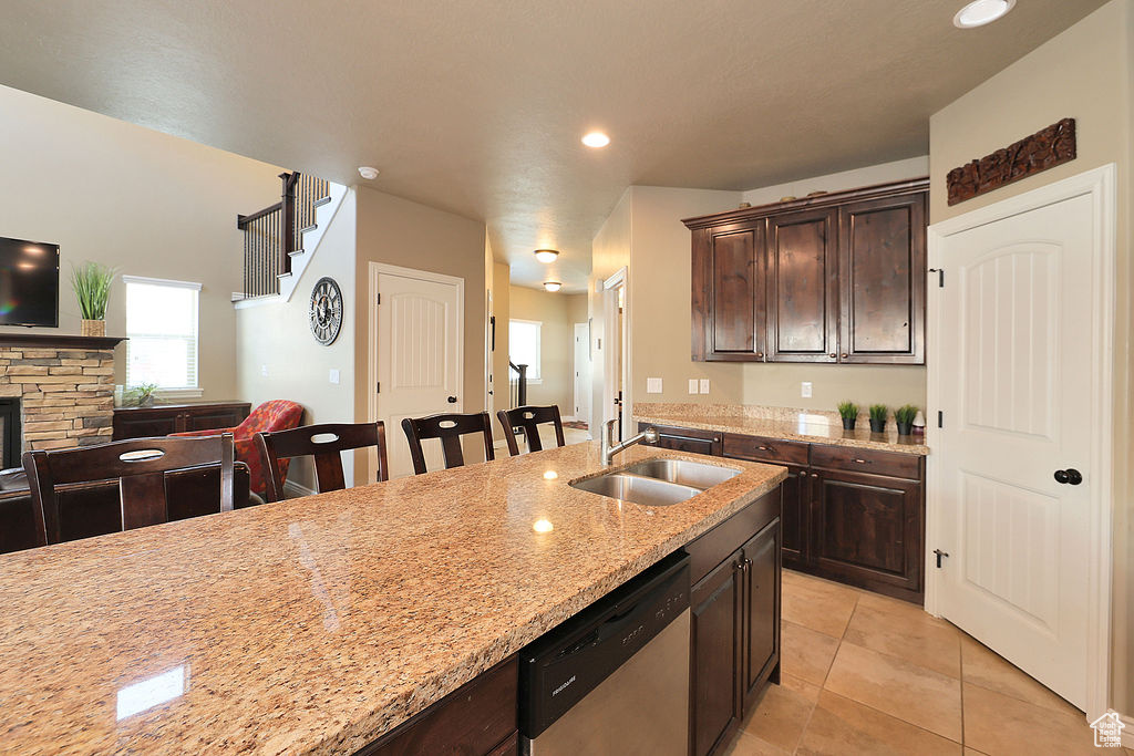 Kitchen featuring stainless steel dishwasher, a kitchen breakfast bar, light tile floors, a fireplace, and sink