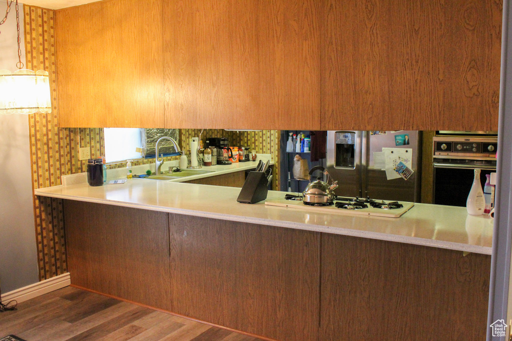 Kitchen featuring kitchen peninsula, sink, black oven, white gas stovetop, and dark hardwood / wood-style flooring