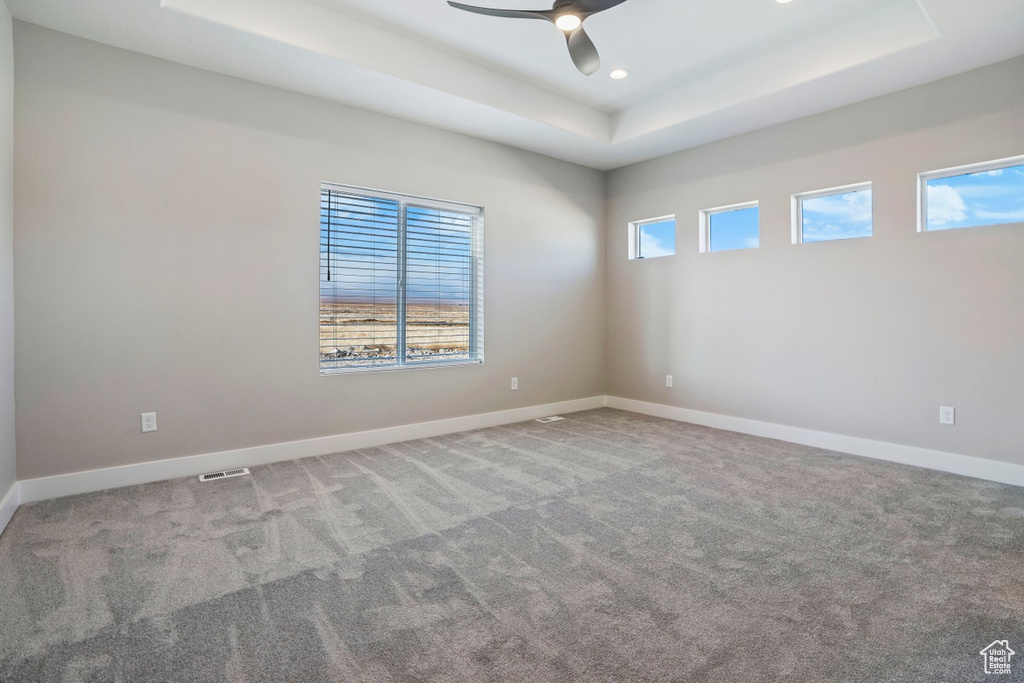 Carpeted empty room featuring ceiling fan and a raised ceiling