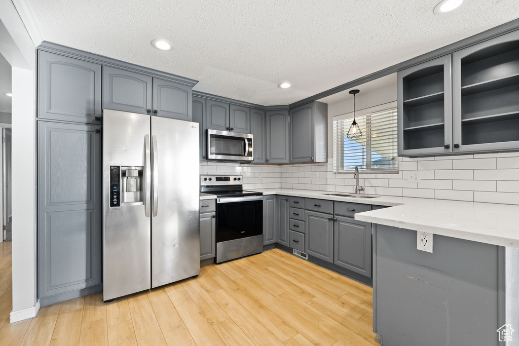 Kitchen featuring decorative light fixtures, light hardwood / wood-style flooring, stainless steel appliances, light stone counters, and tasteful backsplash