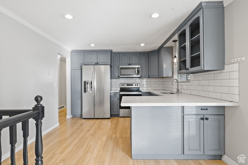 Kitchen featuring gray cabinetry, light hardwood / wood-style floors, tasteful backsplash, and stainless steel appliances