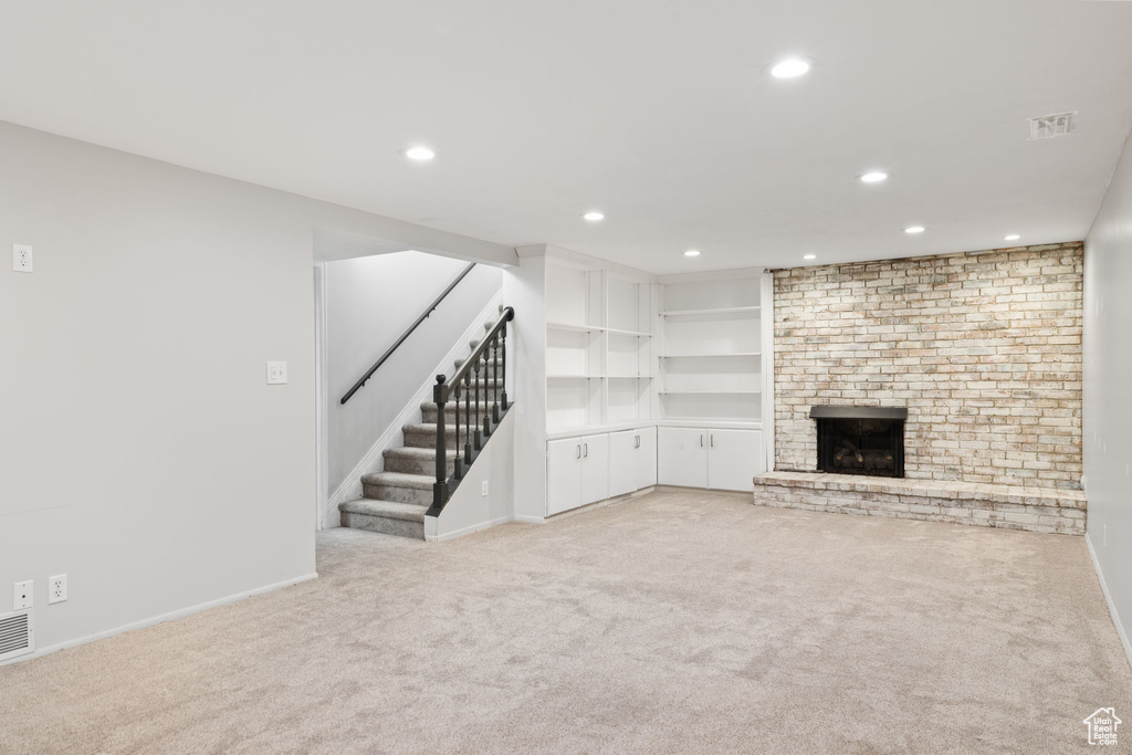 Unfurnished living room featuring light carpet, brick wall, and a fireplace
