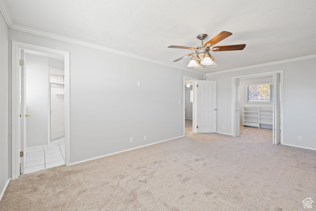 Unfurnished bedroom featuring ensuite bath, crown molding, ceiling fan, and light colored carpet