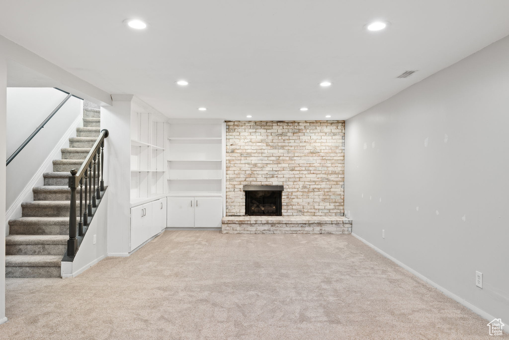 Unfurnished living room featuring light carpet, built in features, a fireplace, and brick wall
