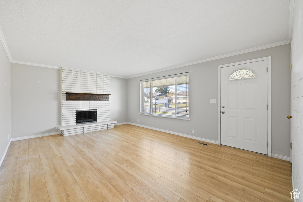 Interior space featuring crown molding, light hardwood / wood-style floors, brick wall, and a fireplace
