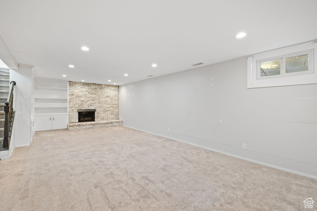 Unfurnished living room with brick wall, light colored carpet, and a brick fireplace