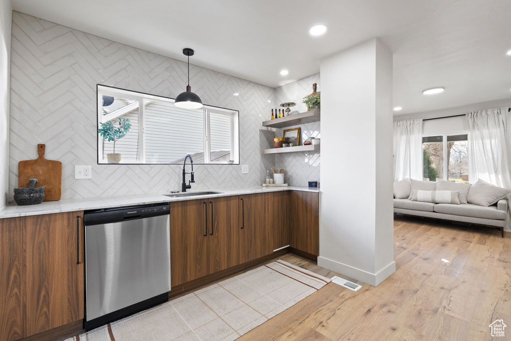 Kitchen with decorative light fixtures, backsplash, light hardwood / wood-style floors, sink, and dishwasher