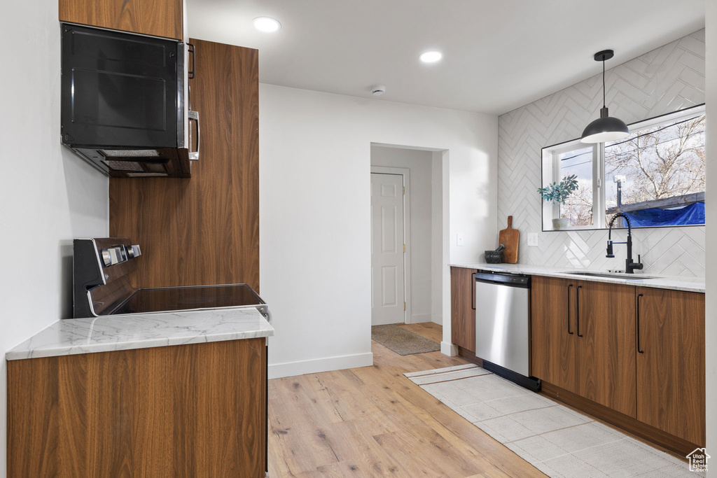 Kitchen with decorative light fixtures, backsplash, sink, light hardwood / wood-style flooring, and dishwasher