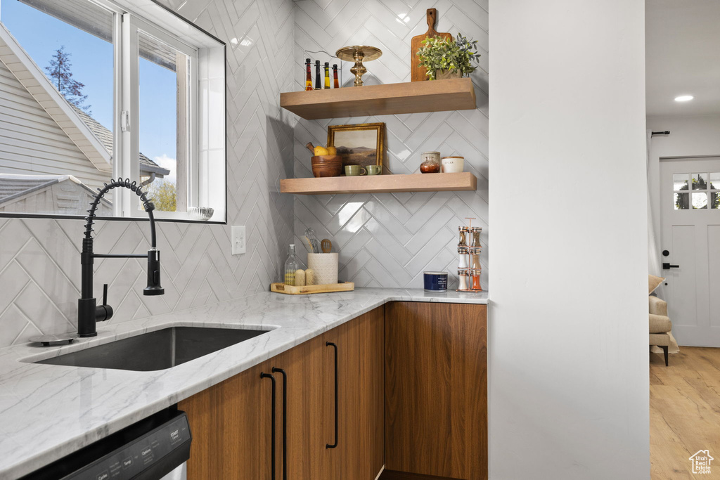 Kitchen with backsplash, light wood-type flooring, dishwashing machine, and light stone counters