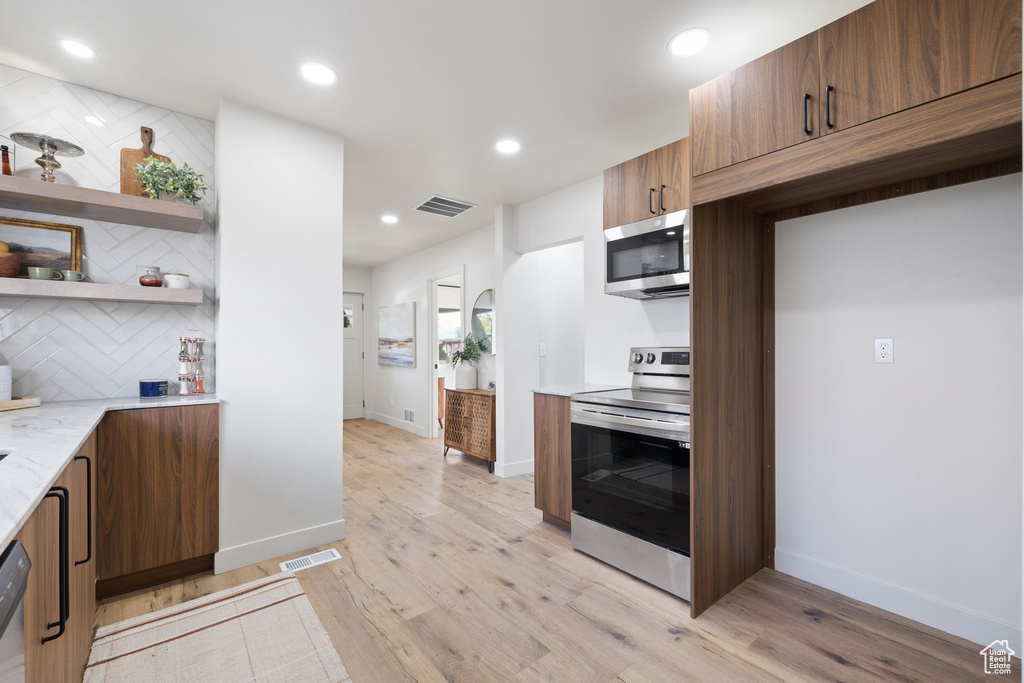 Kitchen featuring light stone counters, tasteful backsplash, stainless steel appliances, and light wood-type flooring