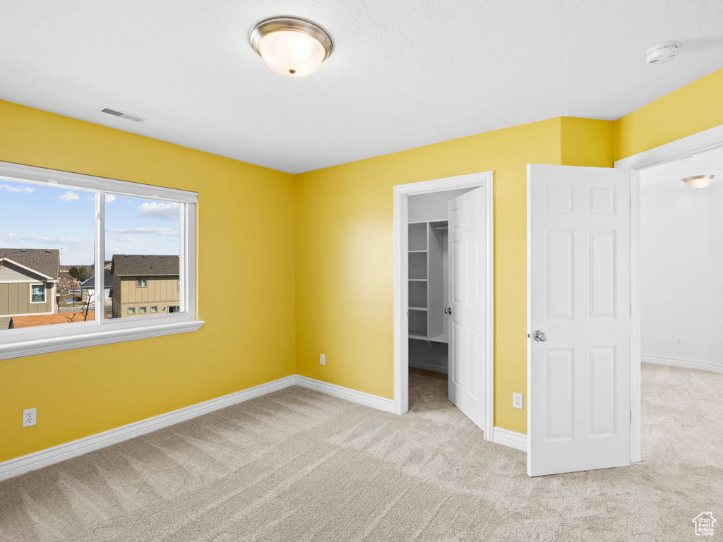Unfurnished bedroom with a closet, a spacious closet, and light colored carpet