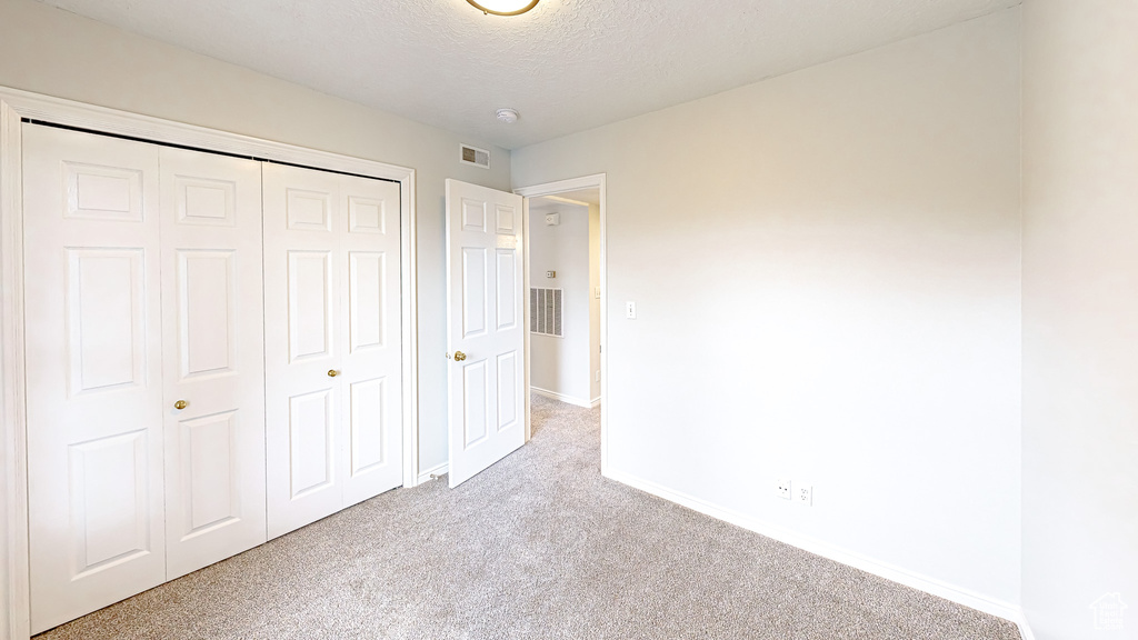 Unfurnished bedroom featuring light carpet, a textured ceiling, and a closet
