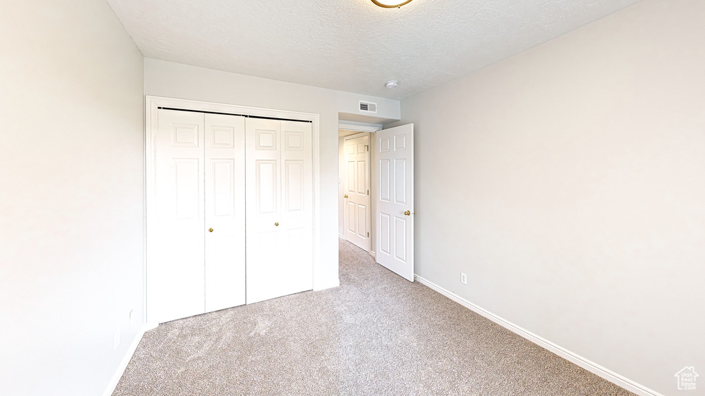 Unfurnished bedroom with light carpet, a textured ceiling, and a closet