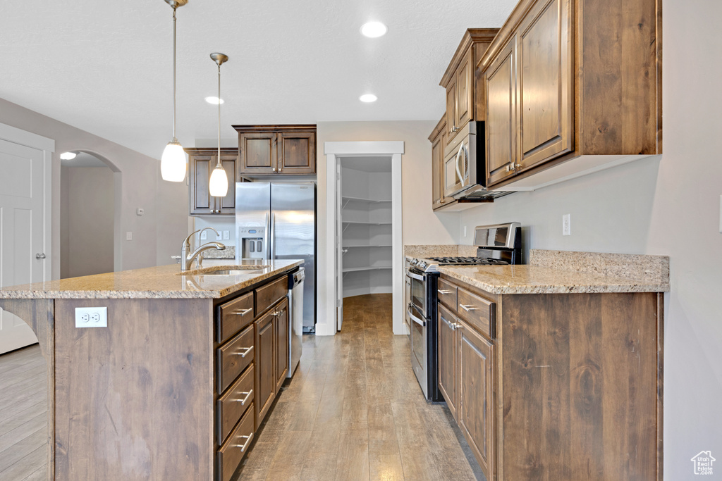 Kitchen with decorative light fixtures, appliances with stainless steel finishes, light hardwood / wood-style floors, a center island with sink, and a breakfast bar area
