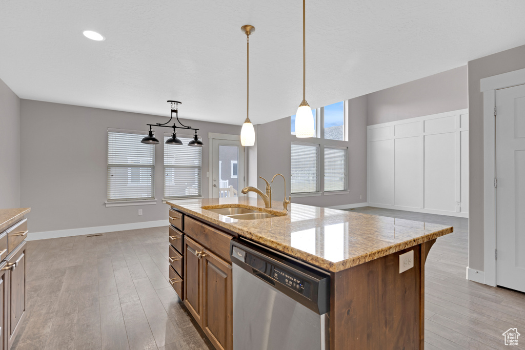 Kitchen featuring light hardwood / wood-style floors, a center island with sink, decorative light fixtures, and stainless steel dishwasher