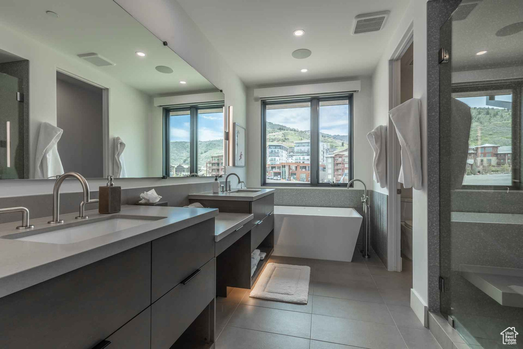 Bathroom featuring plus walk in shower, tile floors, dual sinks, and vanity with extensive cabinet space