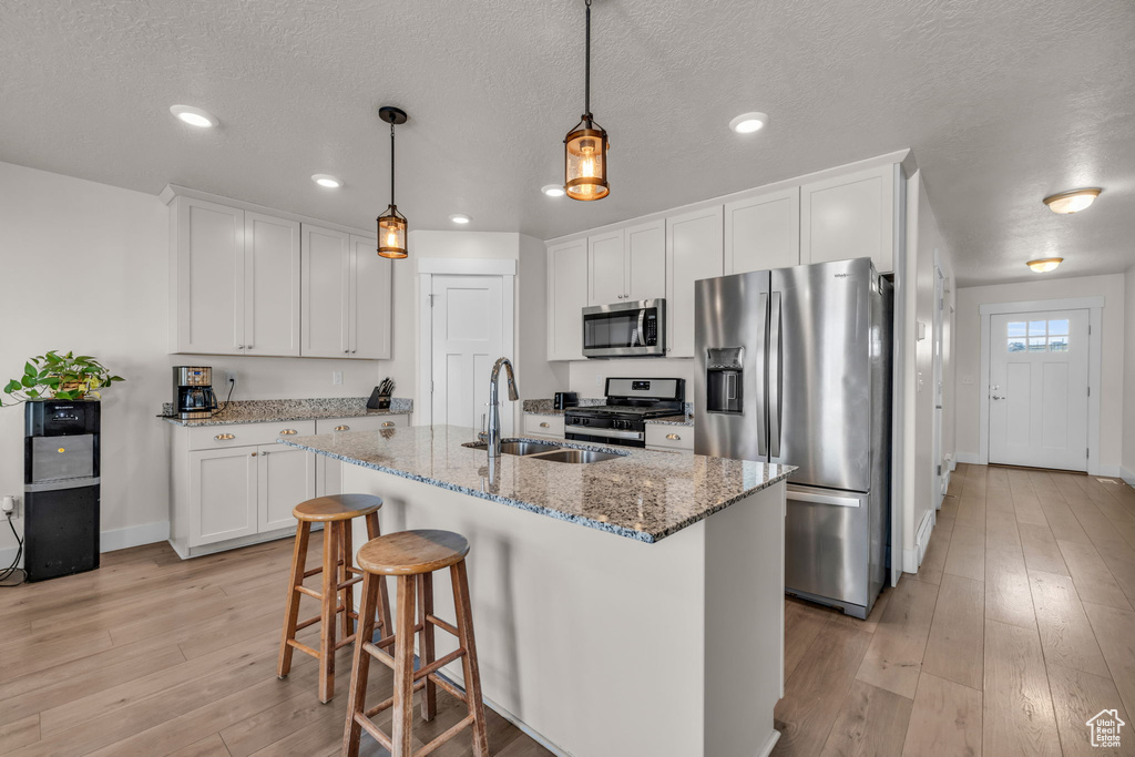 Kitchen featuring decorative light fixtures, stone counters, light hardwood / wood-style flooring, appliances with stainless steel finishes, and white cabinetry