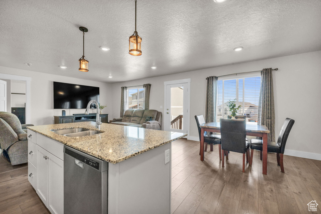 Kitchen with pendant lighting, light hardwood / wood-style flooring, dishwasher, light stone countertops, and white cabinetry