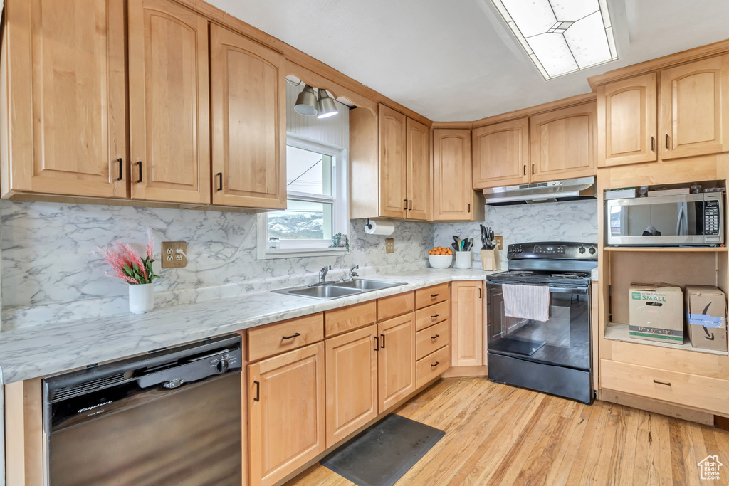 Kitchen with backsplash, light stone counters, black appliances, and light wood-type flooring