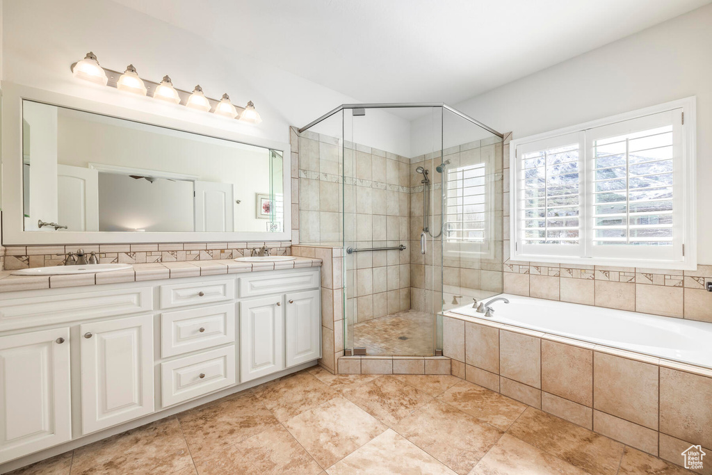 Bathroom with shower with separate bathtub, dual sinks, large vanity, and tile flooring