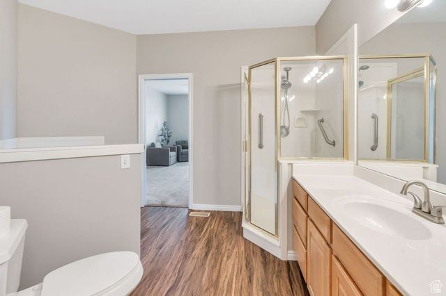 Bathroom featuring toilet, large vanity, hardwood / wood-style floors, and a shower with shower door