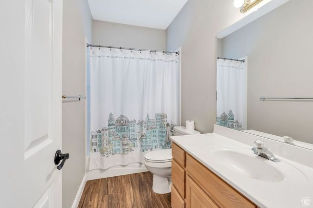 Full bathroom with shower / tub combo, toilet, large vanity, and hardwood / wood-style flooring
