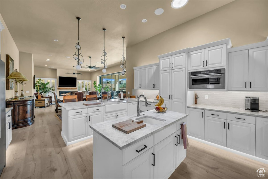 Kitchen with oven, backsplash, light hardwood / wood-style floors, sink, and an island with sink
