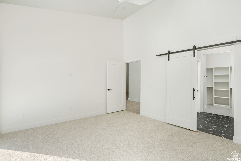 Unfurnished bedroom with a closet, a barn door, a spacious closet, dark colored carpet, and ceiling fan
