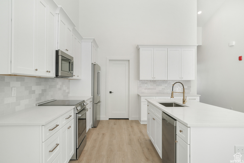 Kitchen featuring light wood-type flooring, premium appliances, sink, tasteful backsplash, and white cabinetry