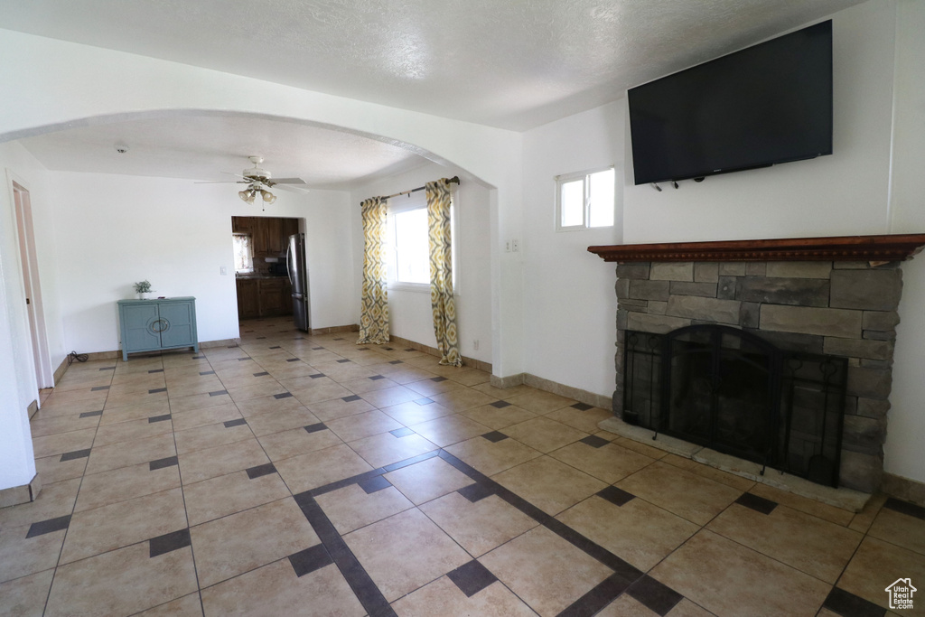 Unfurnished living room featuring tile flooring, ceiling fan, and a stone fireplace