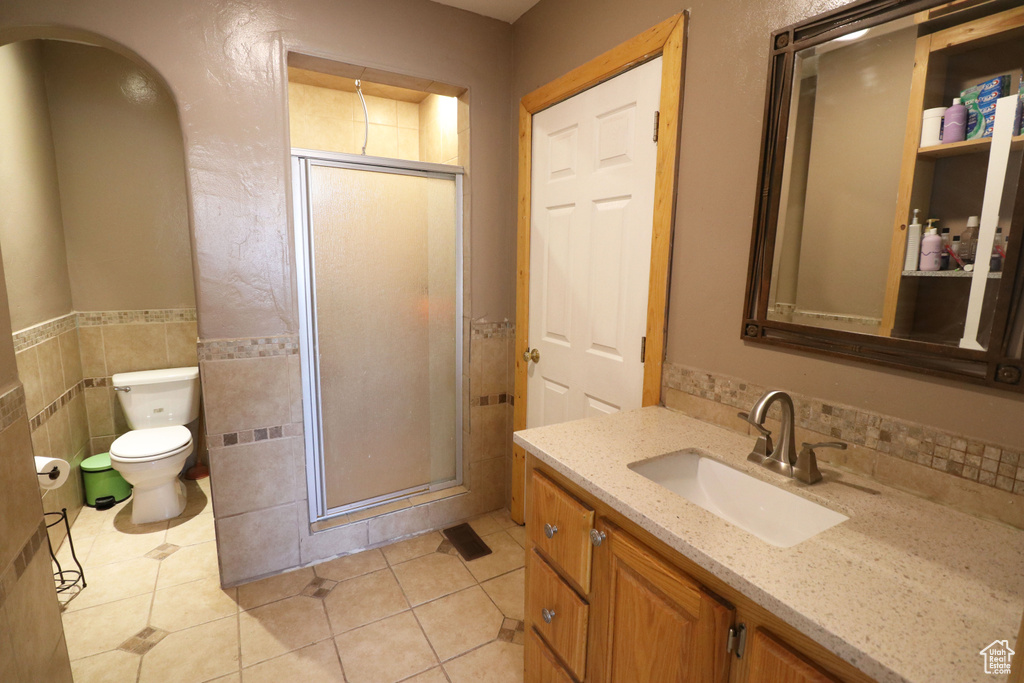 Bathroom with toilet, vanity, tile walls, tile flooring, and an enclosed shower