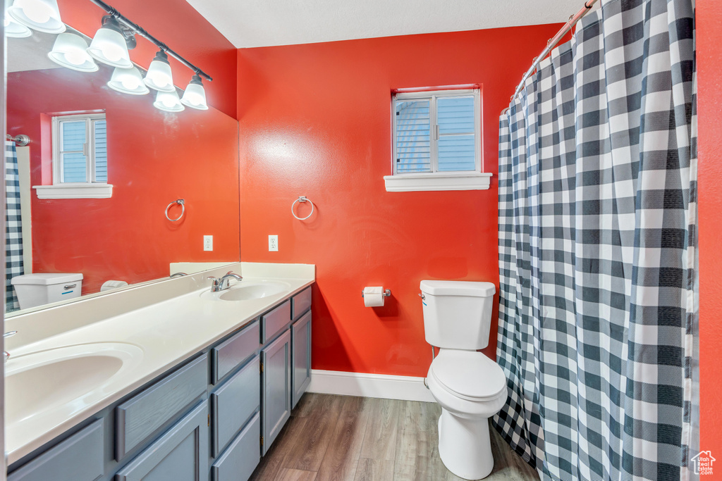 Bathroom featuring oversized vanity, dual sinks, toilet, and wood-type flooring