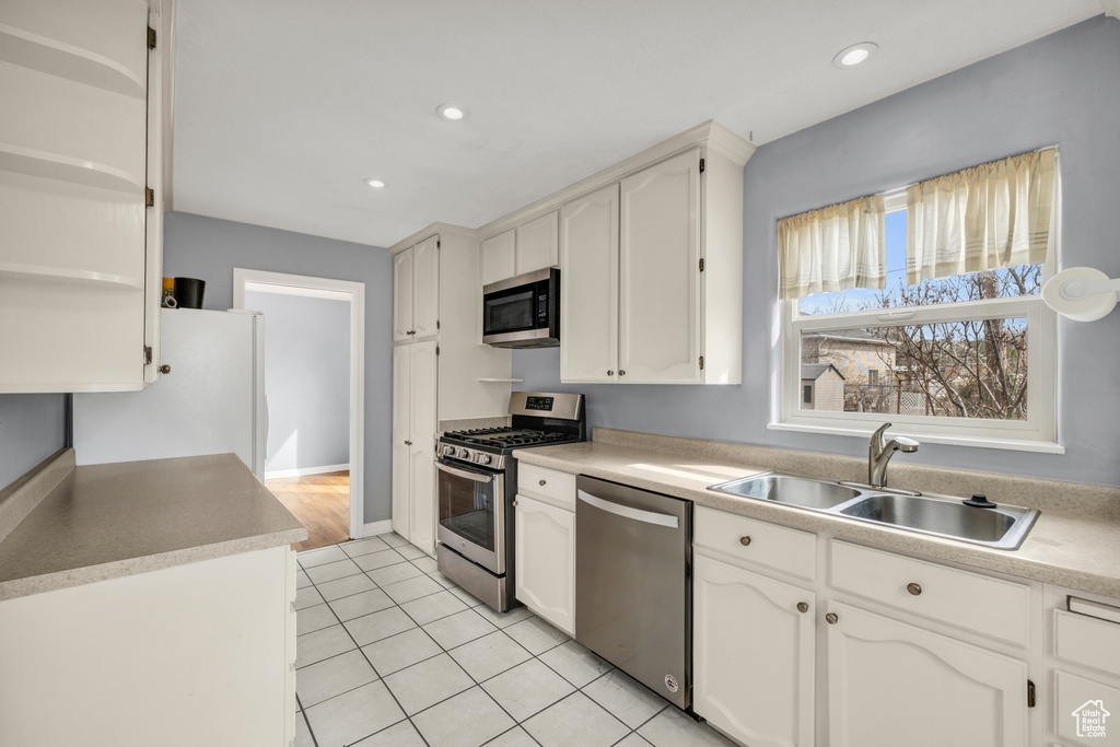 Kitchen featuring appliances with stainless steel finishes, sink, light tile flooring, and white cabinetry