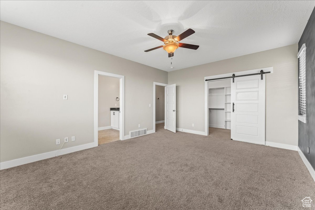 Unfurnished bedroom featuring light carpet, a barn door, a closet, and ceiling fan