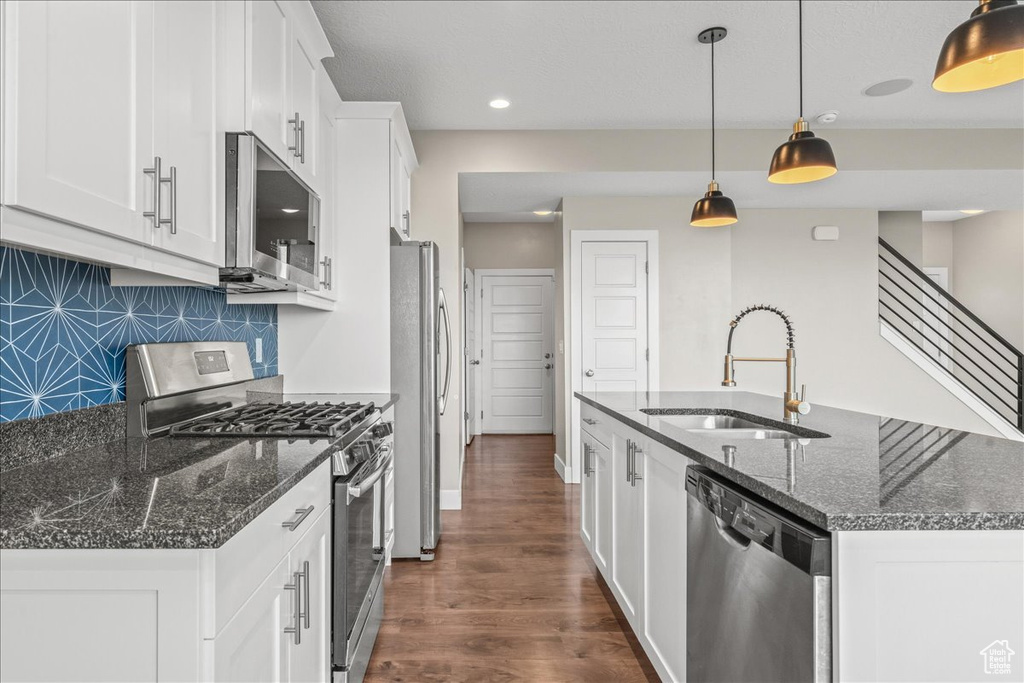 Kitchen with dark hardwood / wood-style floors, pendant lighting, sink, appliances with stainless steel finishes, and tasteful backsplash
